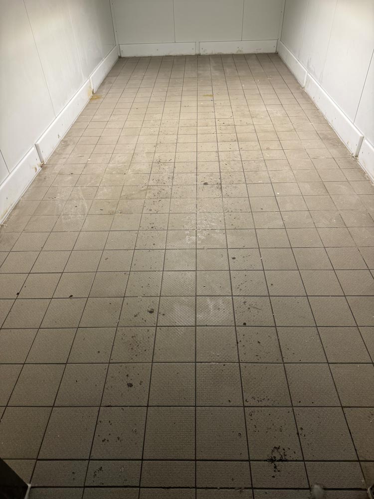 Leerer Raum mit schmutzigem, gefliestem Boden und weißen Wänden.