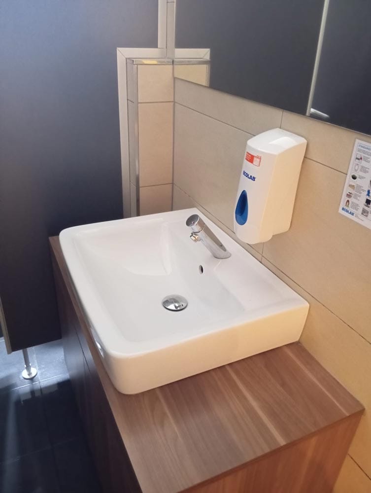 Ein weißes Waschbecken auf einem Holzunterschrank mit Seifenspender an der beigen Wand.