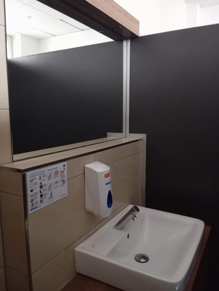 Ein moderner Waschraum mit weißem Waschbecken, Seifenspender und großem Spiegel.