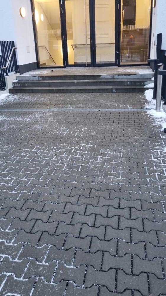 Schneebedeckter Eingang mit Stufen, blauer Tür und erleuchtetem Inneren; keine Personen sichtbar.