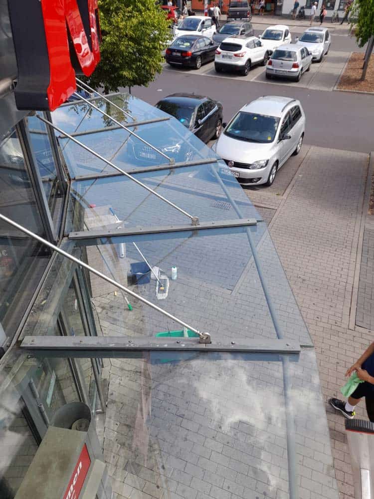 Person kehrt Gehweg; moderne Architektur aus Glas und Metall.