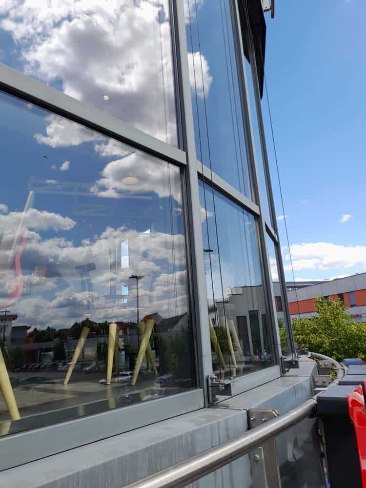 Spiegelung von Wolken auf modernen Glasfenstern eines Gebäudes, blauer Himmel im Hintergrund.