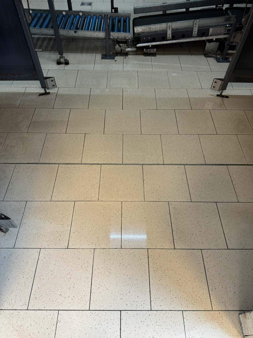 Ein gefliester Boden in einer Fabrik mit Maschinen und Förderband.