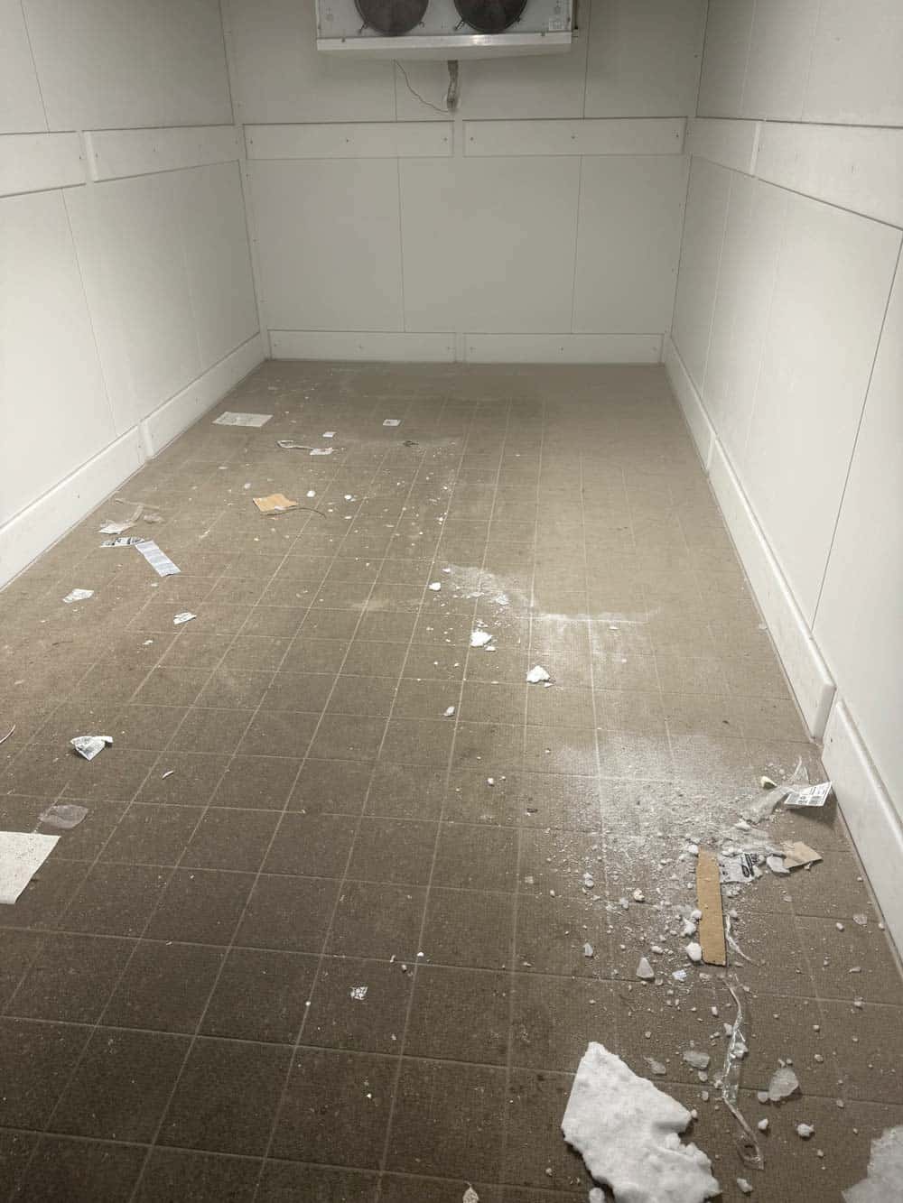 Ein leerer Raum mit weiß gestrichenen Wänden und einem Boden mit verstreutem Müll.