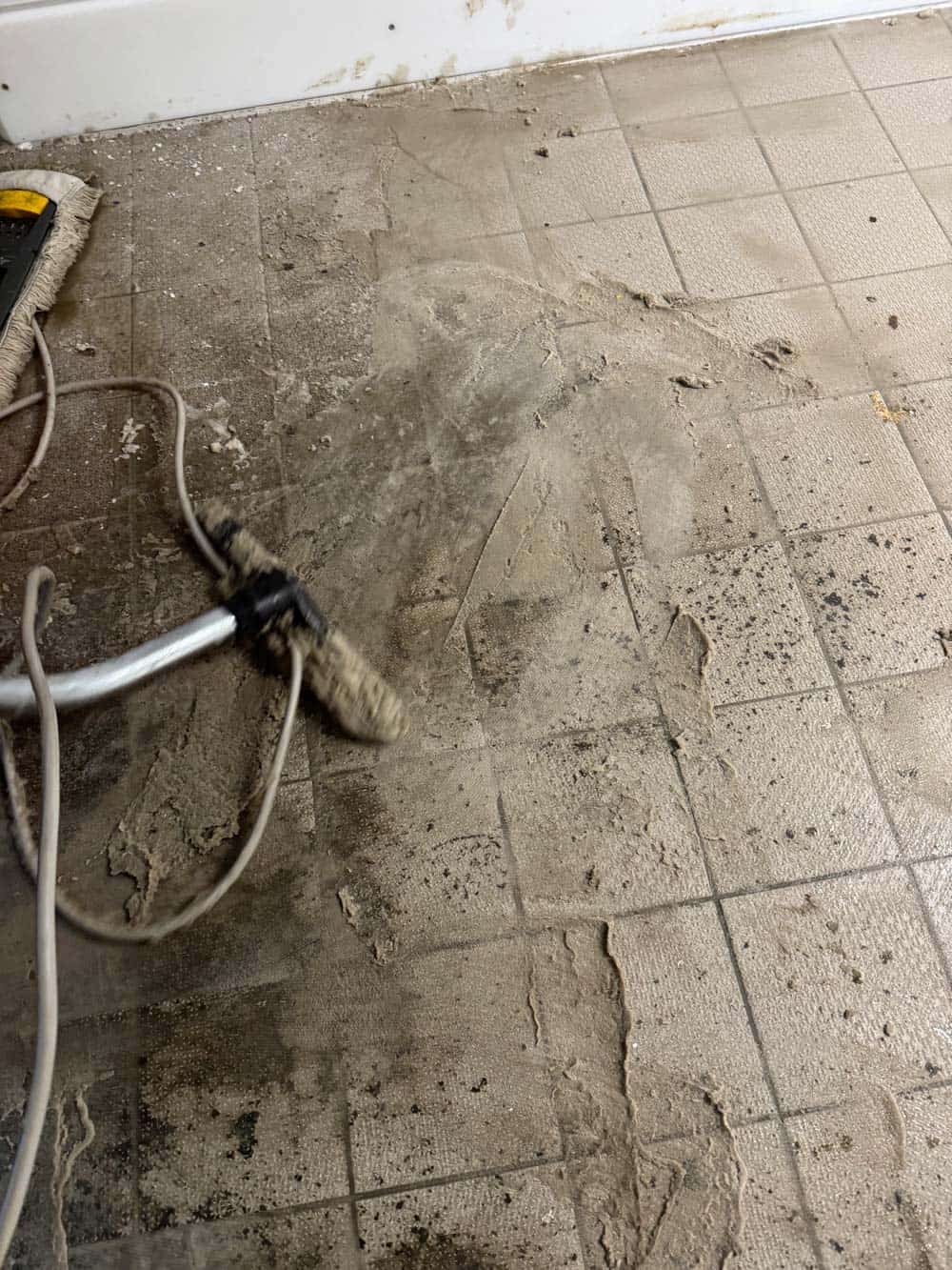 Ein Boden wird mit einem Reinigungsgerät von Schmutz befreit. Beige Fliesen, staubige Oberfläche.