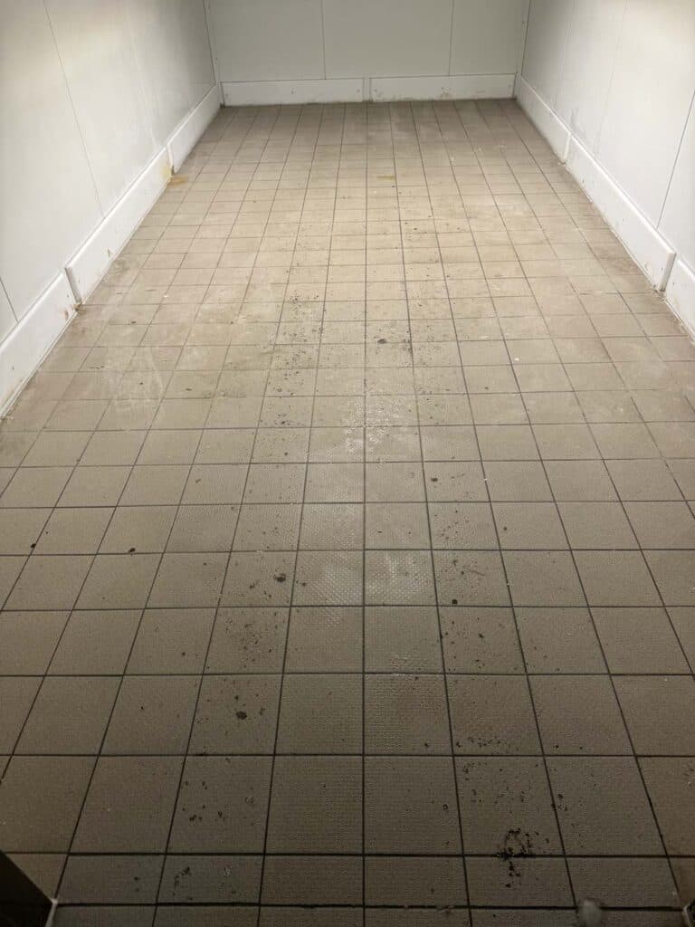 Leerer Raum mit beigem Fliesenboden, Schmutzflecken verteilt. Weiße Wände.